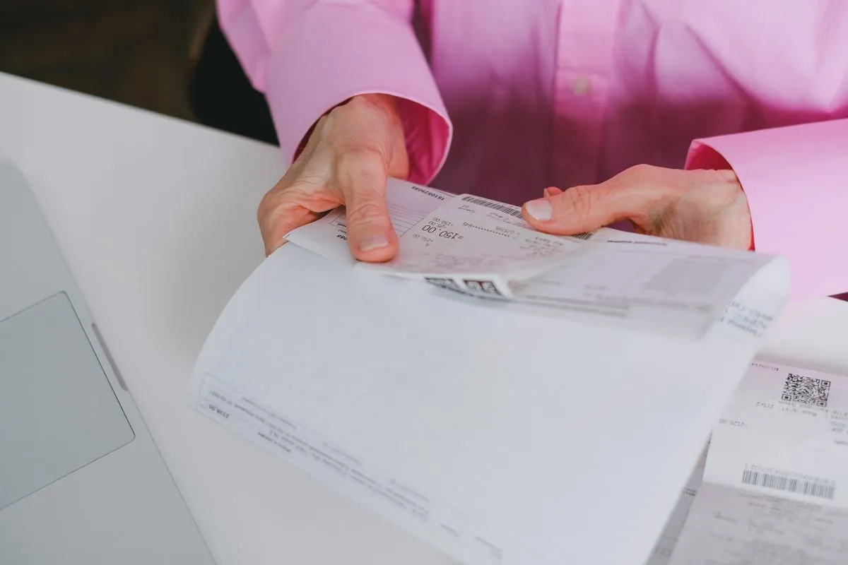 Pessoa manuseando e organizando recibos e notas em papel, mantendo o histórico em ordem