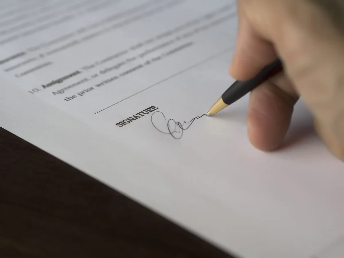 Mão assinando um contrato com caneta sobre a mesa de madeira
