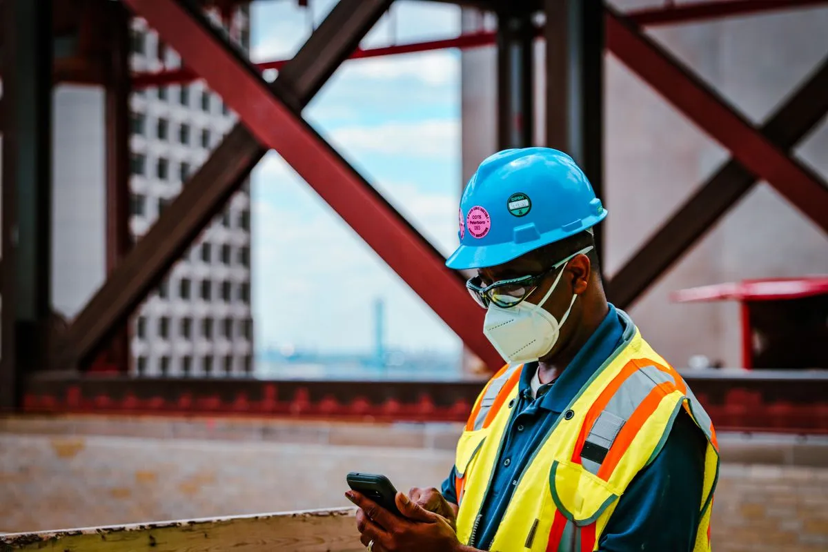 Técnico com equipamento de proteção usando o celular em campo na obra