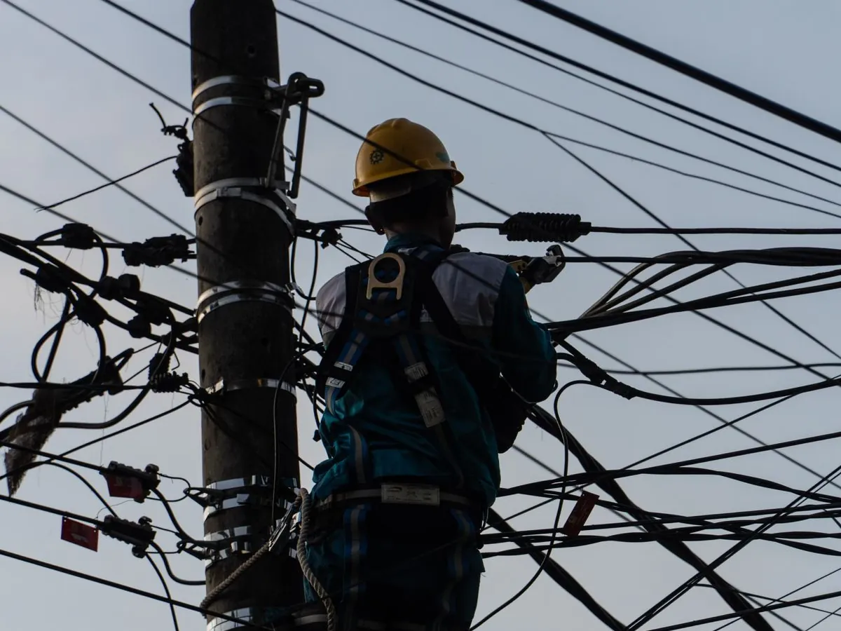 Técnico com capacete e cinto de segurança trabalhando em cabos no alto de um poste